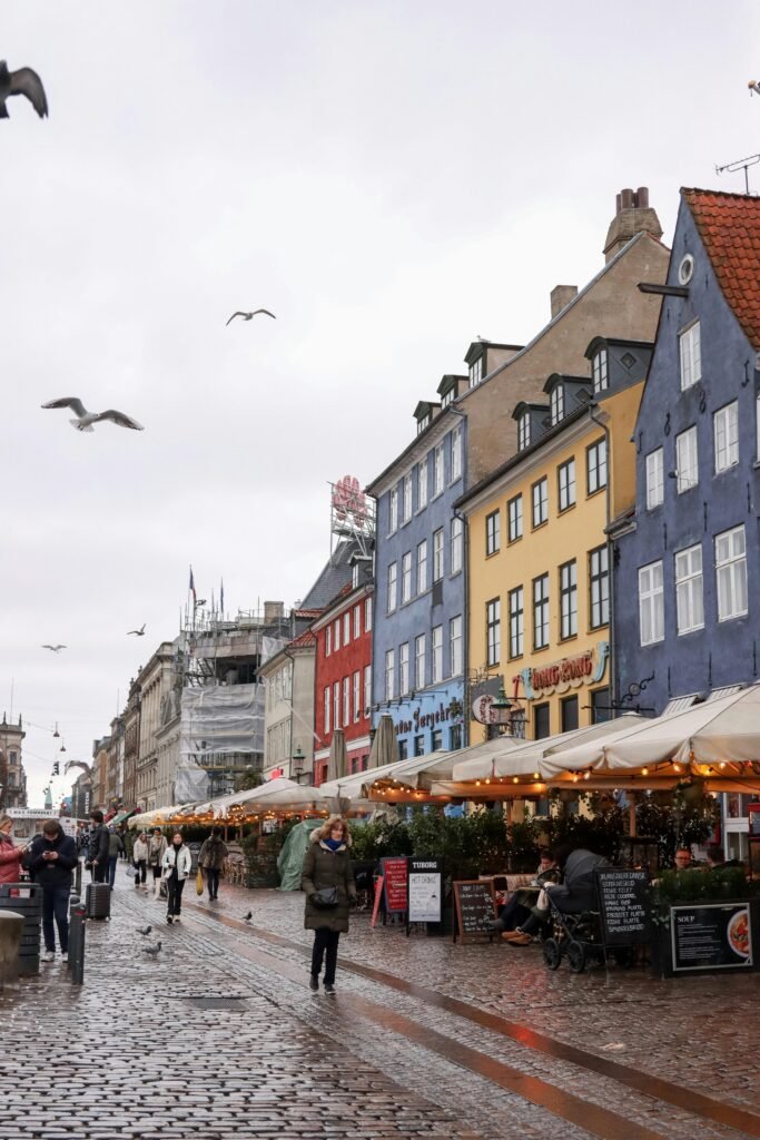Vibrant Nyhavn in Copenhagen with colorful buildings and bustling street life on a cloudy day.